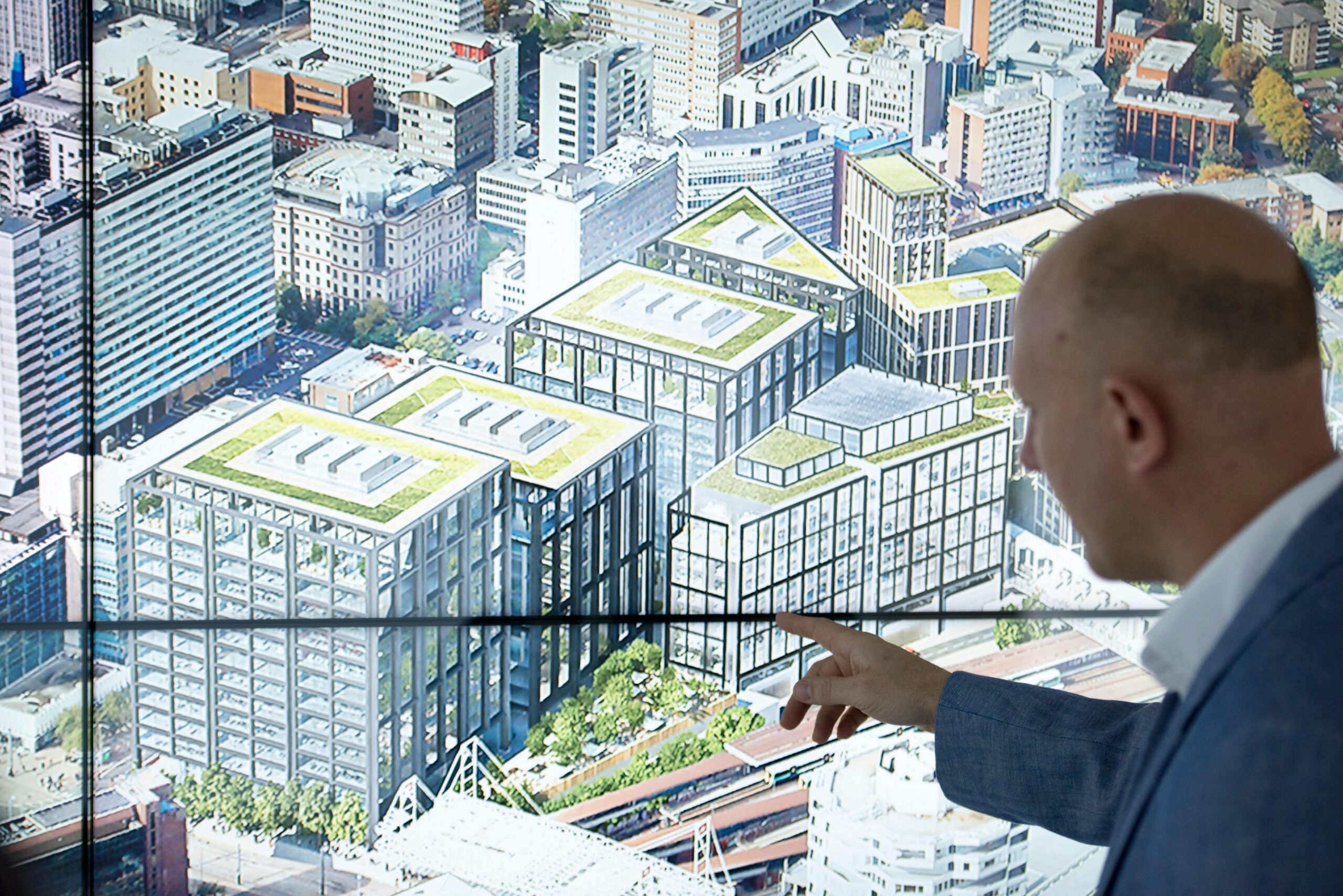 man looks and points at screen showing builldings